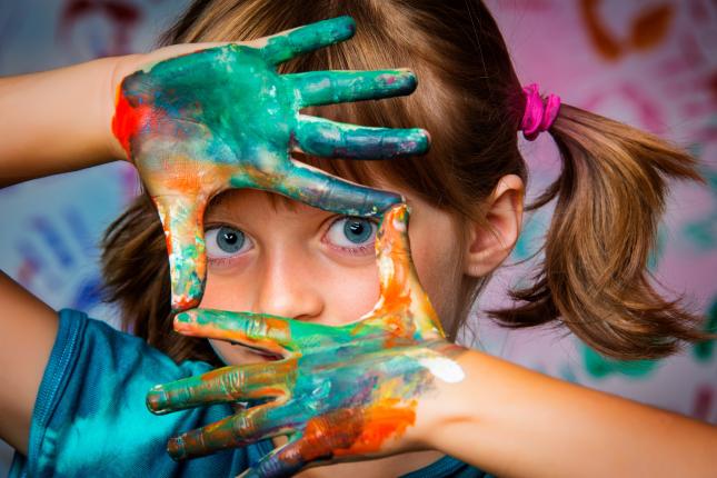 Girl looks through hands painted with paint